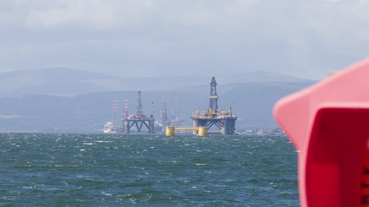 Distant offshore oil platform seen from boat, partial red railing, daylight, slight camera panning motion