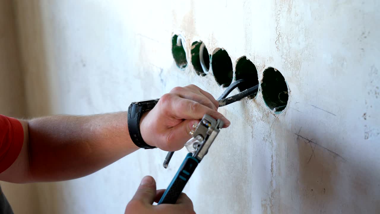 Male worker with pliers cleaning wires in junction box for socket