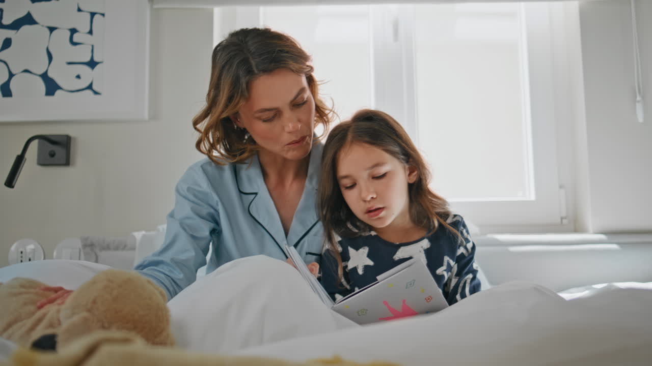 Cute girl watching book with parent at home closeup. Happy family reading in bed