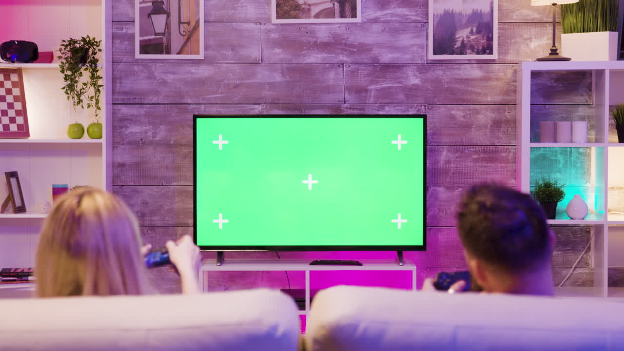 Couple playing video games on a TV with a green screen in their living room