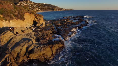 Vista-Aérea-De-Drones-De-Personas-Explorando-Formaciones-Rocosas-Frente-Al-Mar-En-Laguna-Beach,-California