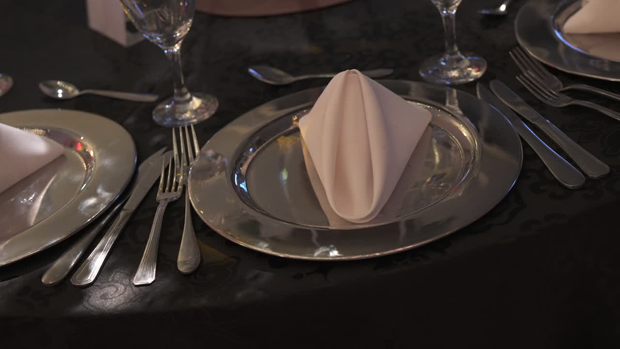 정식 식사 경험을 위해 정교한 테이블 배열을 만드는 실버웨어와 유리 용품과 함께 충전판에 접힌 킨을 특징으로하는 우아한 장소 설정.