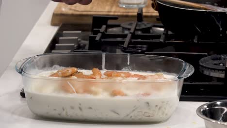 a flavorful shrimp casserole is being prepared in a modern kitchen. succulent shrimp are added to a creamy sauce with fresh herbs, creating a mouthwatering dish ideal for gatherings