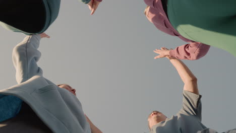 팀원들이 연합과 협업으로 함께 손을 치는 위쪽 시선, 야외 환경에서 팀워크, 에너지 및 집단 노력의 순간을 포착합니다.