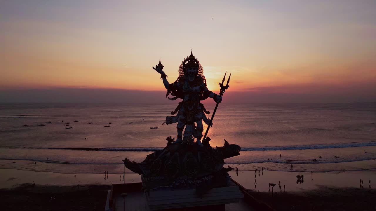 Aerial footage captures Kuta Beach at sunset with the majestic Baruna statue standing as a cultural landmark, highlighting Bali’s coastal beauty and rich artistic heritage from above
