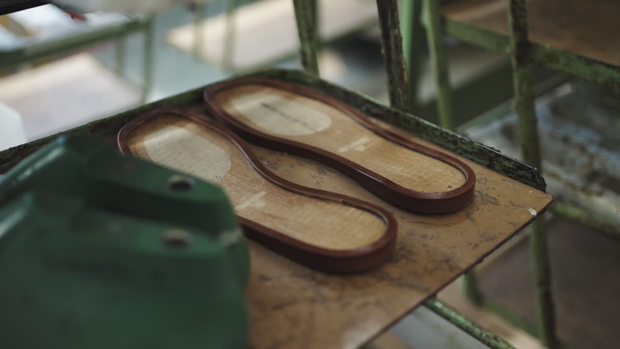 Freshly glued sandal soles resting on an aged industrial rack of factory line