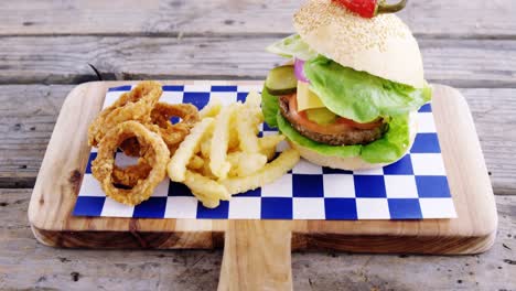 hamburguesa, anillo de cebolla y papas fritas en la tabla de cortar