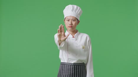 asian woman chef looking at camera and disapproving with no hand sign in the green screen background studio