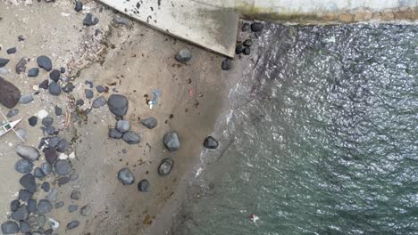 Birdseye-view-of-rocky-beach,-swimmers,-and-coastal-bike-path-road