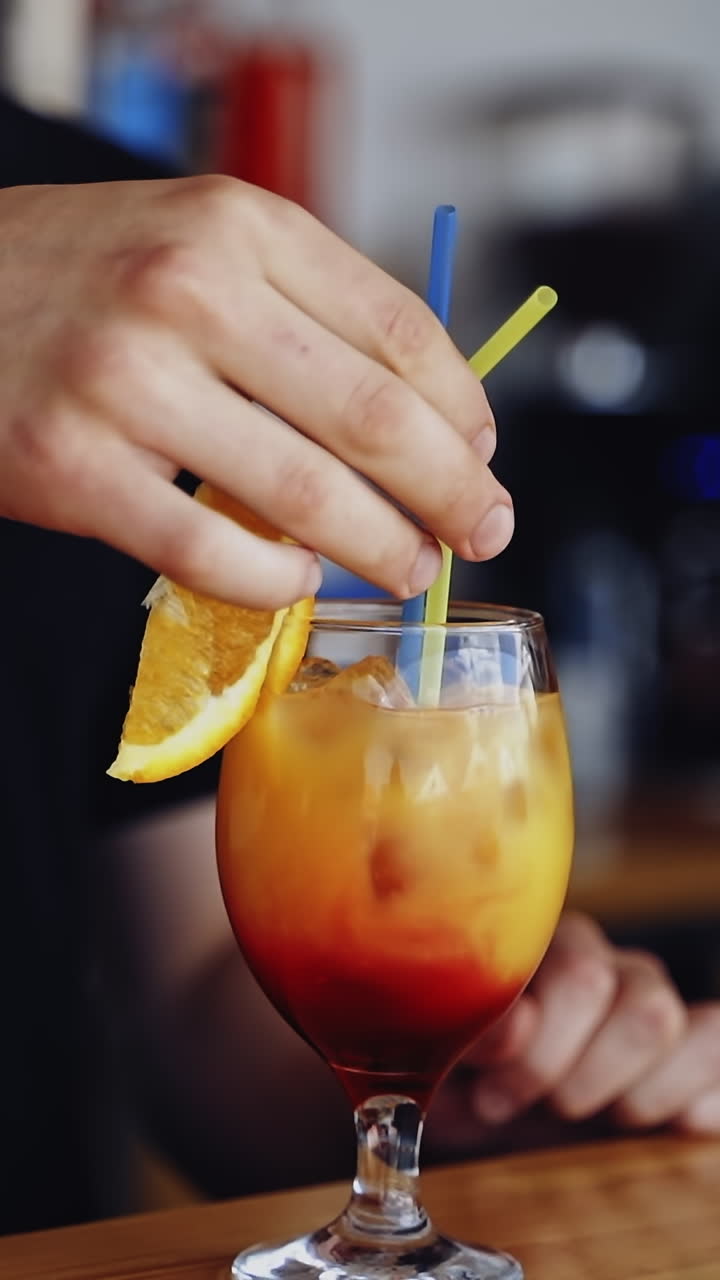 Tasty cocktail in glass. Bartender cooks the beverage for client. Fresh alcohol drink ready on a bar table. Slice of orange on a glass with color liquid with ice. Vertical video