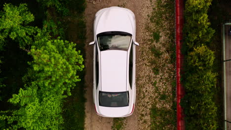 medium wide top down aerial drone shot of white car driving down dirt driveway into a car garage attached to a home