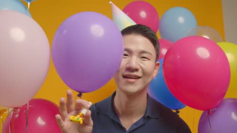 studio portrait of man wearing party hat celebrating birthday with balloons and party blower 3