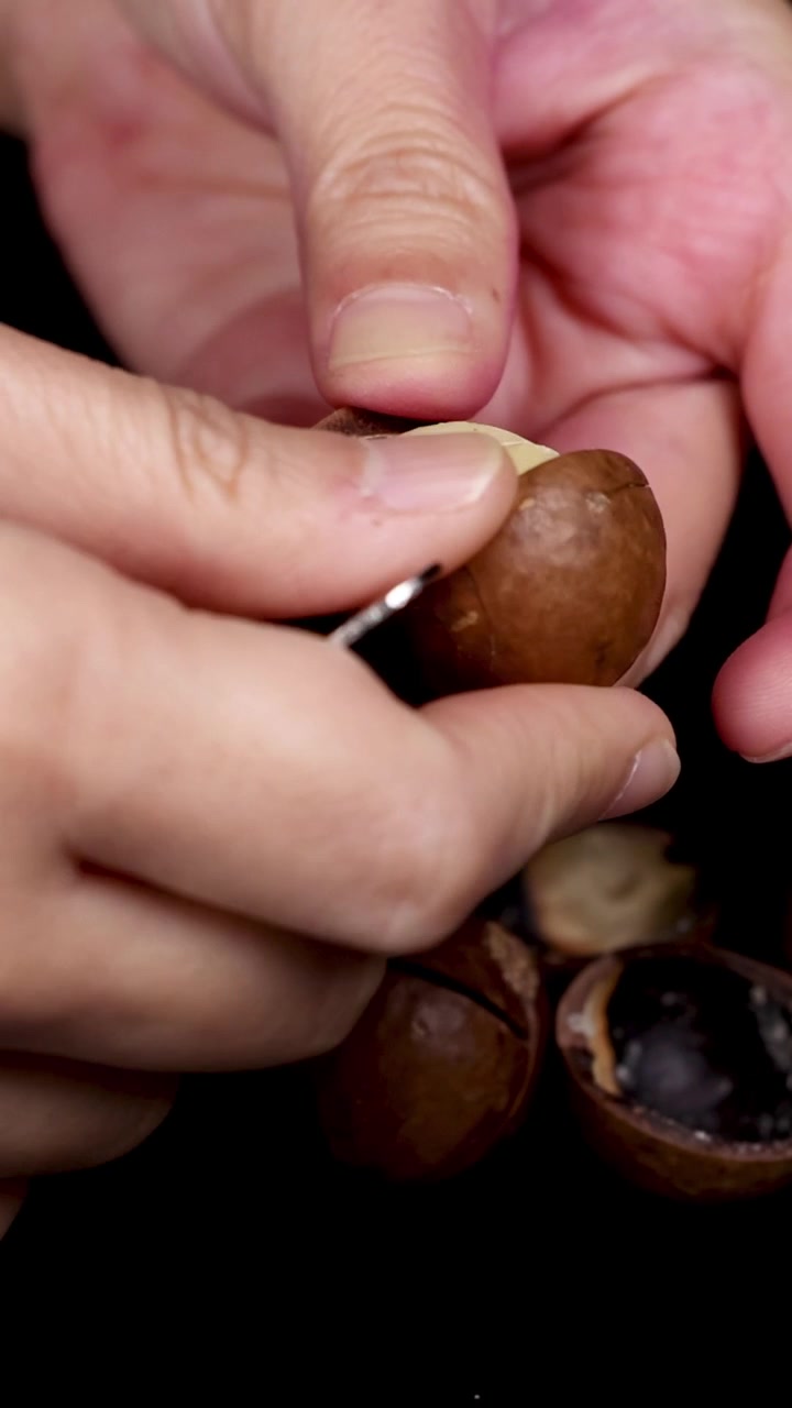 Mani che rompono e rivelano noci di macadamia