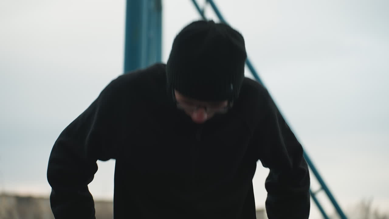 Close-up of a young boy working out on a metal bar, dressed in a black outfit and glasses