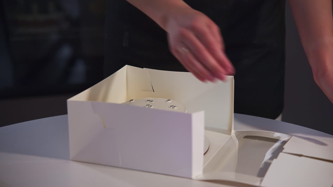 Hands Packaging a Small White Cake with Sprinkles into a Box