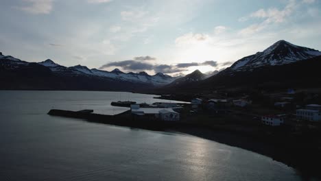 Aerial-reveal-shot-of-a-small-town-in-East-Iceland-surrounded-by-mountains-during-sunset