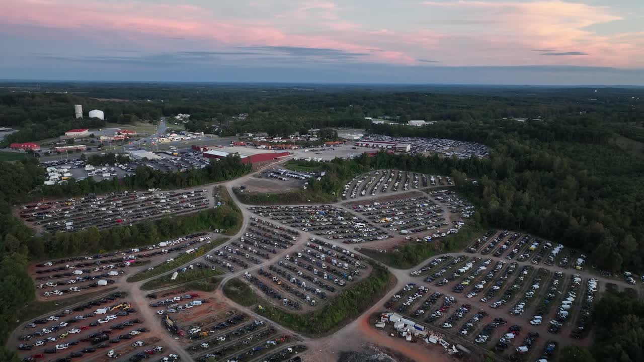 Large American scrapyard or junkyard with crowd of destroyed vehicles in row. Sunset time in USA. Green industrial suburb district of town. Drone wide shot