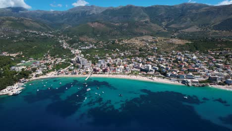 Bahía-Panorámica-Junto-Al-Mar-En-La-Ciudad-Costera-De-Himara,-Playa-Bañada-Por-Las-Aguas-Azules-Del-Mar-Jónico,-Ciudad-Acogedora-Para-Los-Turistas-De-Vacaciones-De-Verano