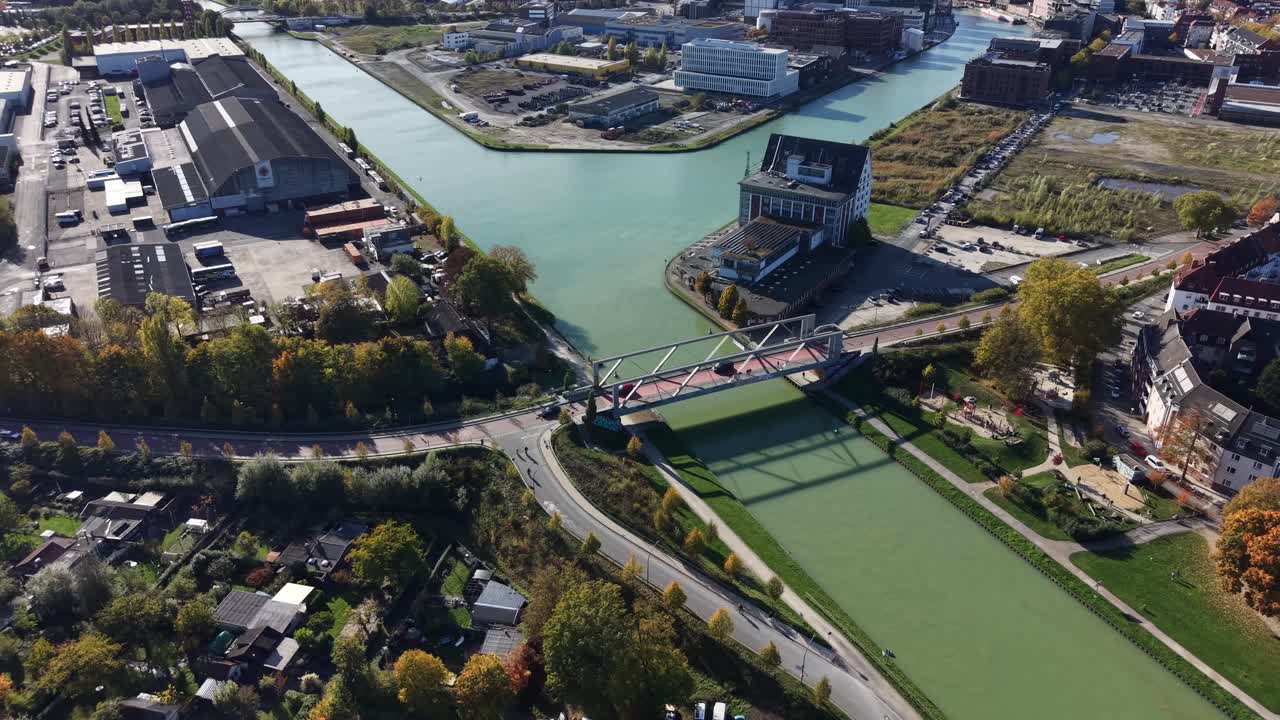 Münster, Germany with industrial buildings, waterways, modern structures and bridges shaping. Harbor district while trees and paths line of canals under clear daylight. Aerial wide shot