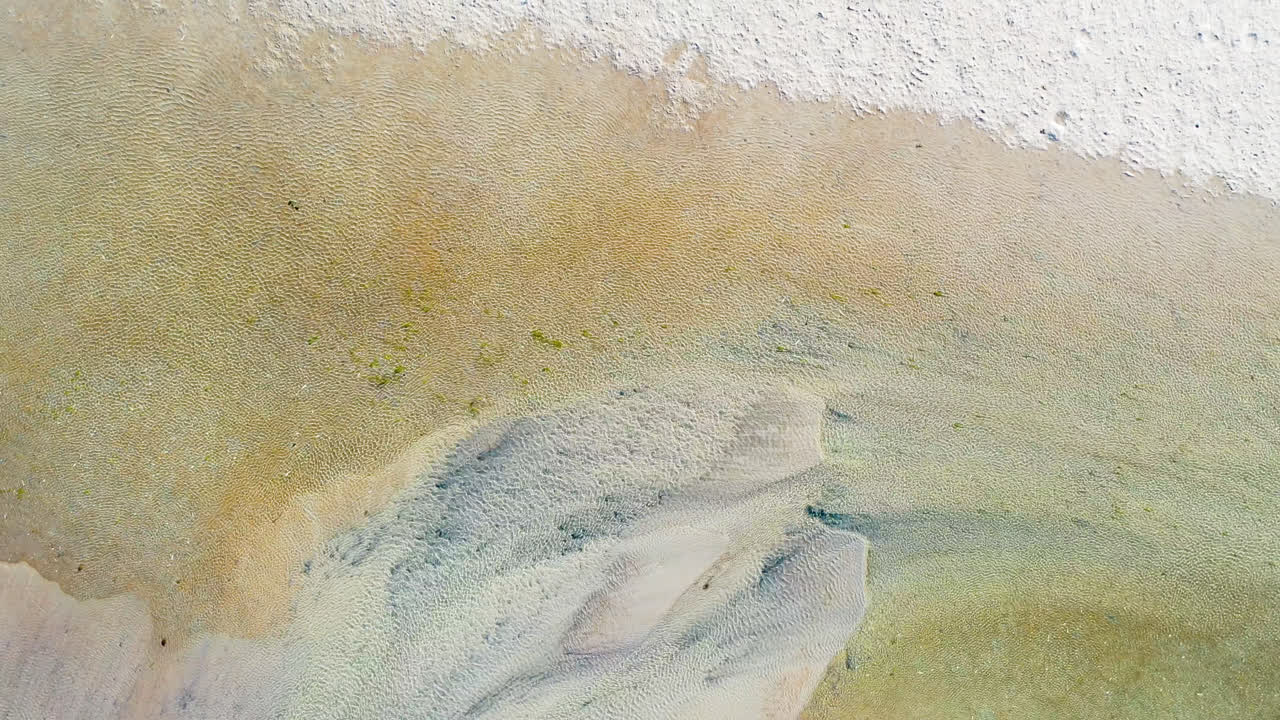 바람에 파도가 부는 얕은 바다 해변과 모래의 무인 항공기 공중 상승 및 느린 회전 공개