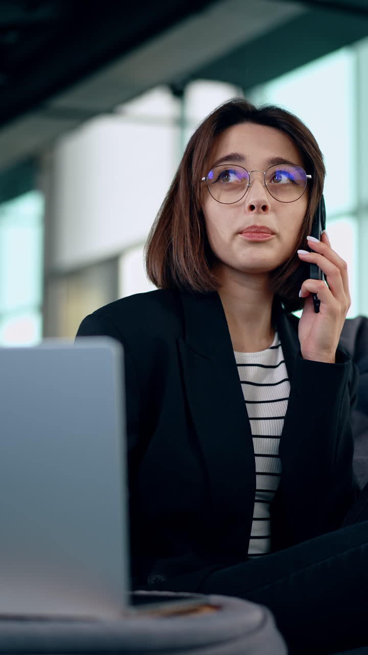 Female entrepreneur wearing glasses speaking on the phone. Portrait of a positive Caucasian lady at work. Vertical video.