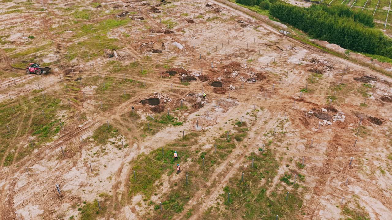 Imagem aérea mostra engenheiros de capacete inspecionando futuro campo de energia solar