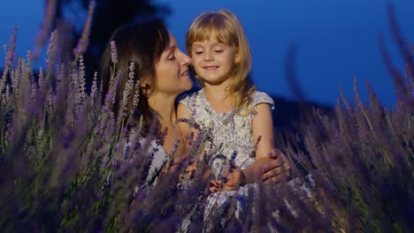 Mother-and-girl-daughter-kid-kissing,-laughing-in-aromatic-flowers-lavender-field-garden-at-night