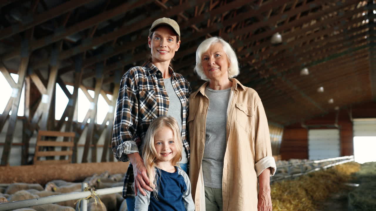 retrato de abuela caucásica, madre y niña sonriendo a la cámara en un establo con rebaño de ovejas
