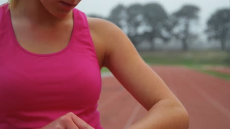 Vista-Frontal-De-Una-Joven-Atleta-Caucásica-Usando-Un-Reloj-Inteligente-En-Un-Recinto-Deportivo-4k