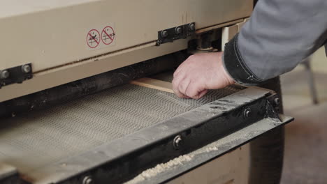 a carpenter uses a drum sander and removes the finished plank of wood from the conveyor belt