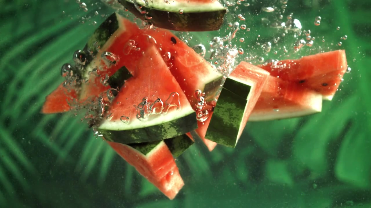 Fette di anguria fresca che si tuffano nell'acqua con sfondo verde
