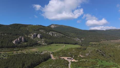 forward drone flight over rural valley with rocky hills, pine-covered slopes, scattered farms and clear skies in a peaceful natural setting