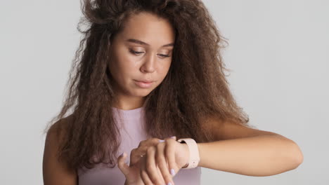 una mujer caucásica de cabello rizado revisando las notificaciones en su reloj inteligente.