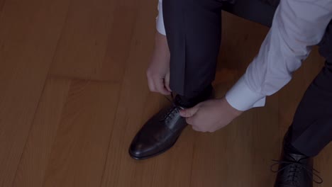close up of groom tying black dress shoes over polished wooden floor