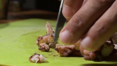 las manos del hombre cortan el pulpo hervido en pedazos para hacer comida de mar en casa, de cerca