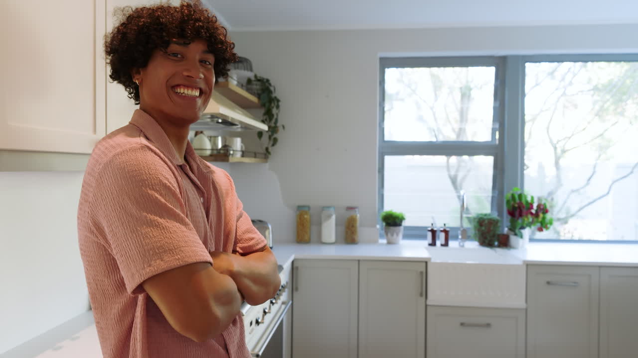 Smiling man standing in modern kitchen with arms crossed, enjoying bright morning, at home