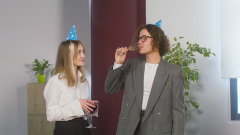 Niño-Y-Niña-Felices-Con-Gorro-De-Fiesta-Bebiendo-Y-Hablando-Juntos-En-La-Fiesta-De-La-Oficina