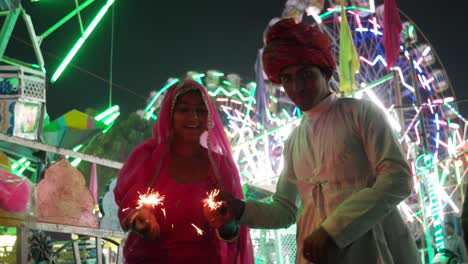 indian couple in traditional dress with fire sparkle cracker at diwali mela festival in india