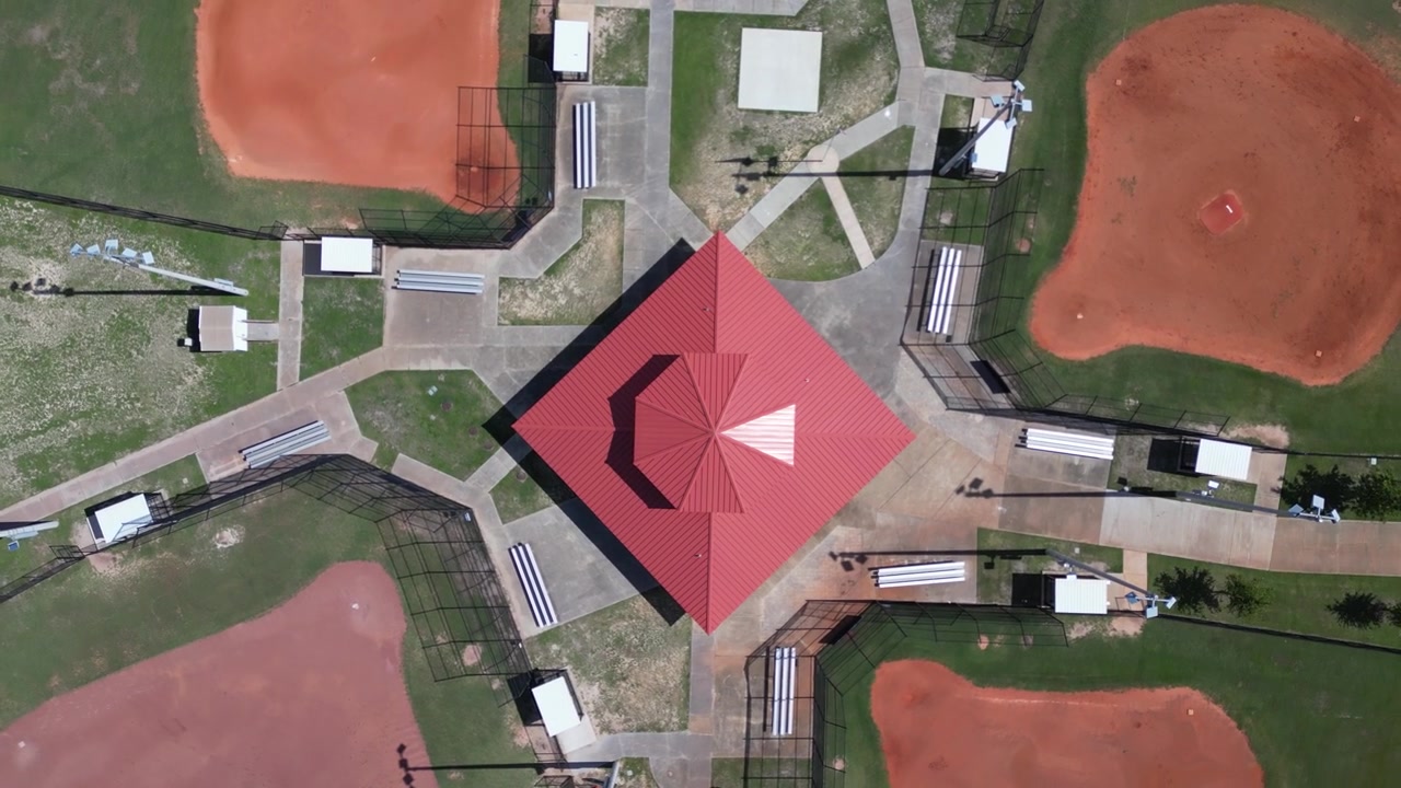 Slowly rising and spinning drone shot looking straight down at concession building between baseball fields at a small sports park.