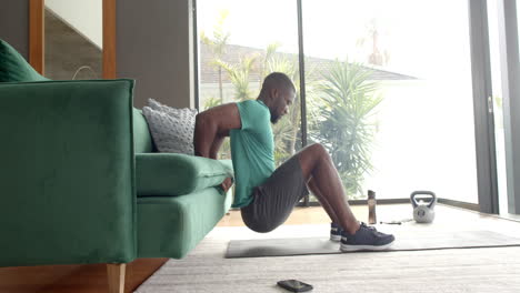 strong and fit man doing tricep dips using sofa at home, exercising indoors