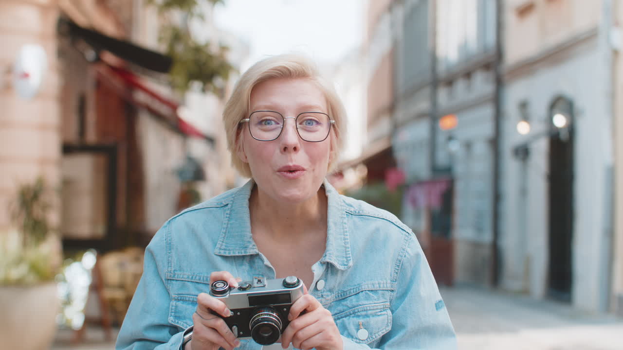 Portrait of happy young woman tourist traveler taking photos using retro camera on city urban street