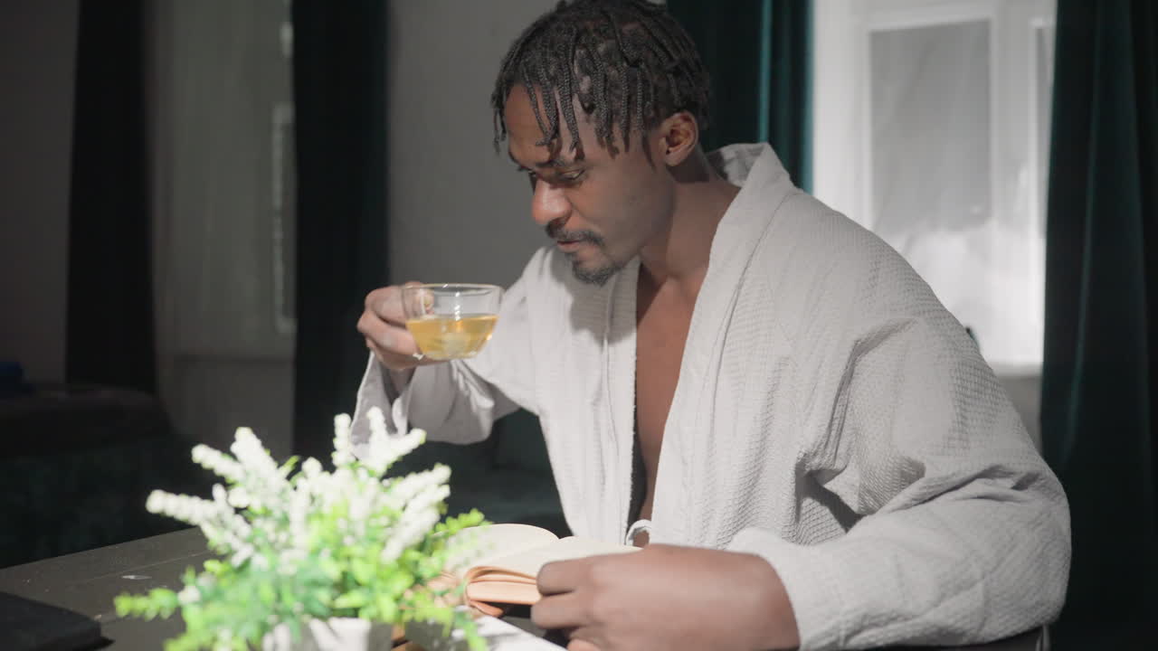 Champ enjoying tea and reading book in cozy home setting. Relaxed, mindful morning with plant decor, bright sunlight, and calming atmosphere. Ideal for self-care, quiet moments, and peaceful routines