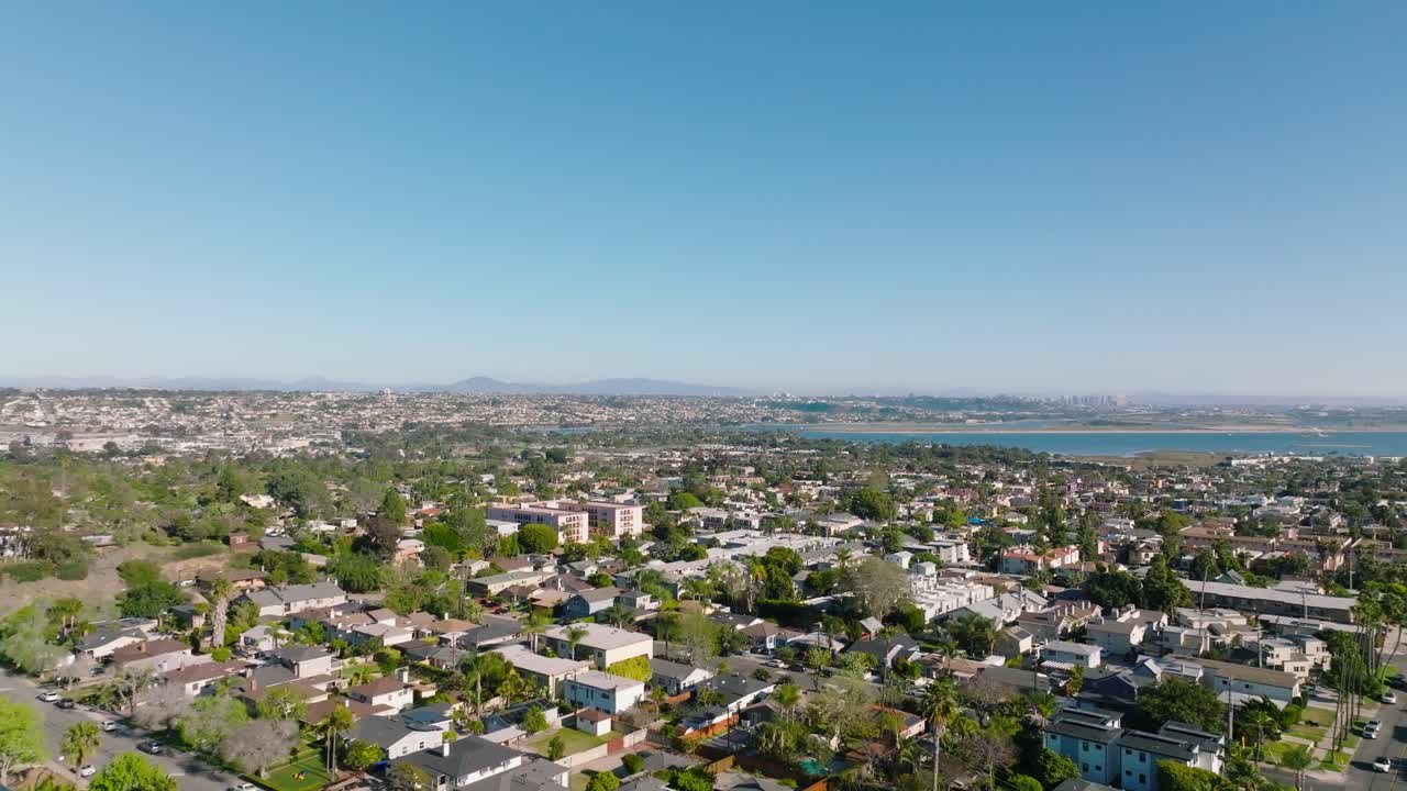 Sweeping aerial view over Pacific Beach, showing rows of coastal homes and palm tree-lined streets with ocean in distance