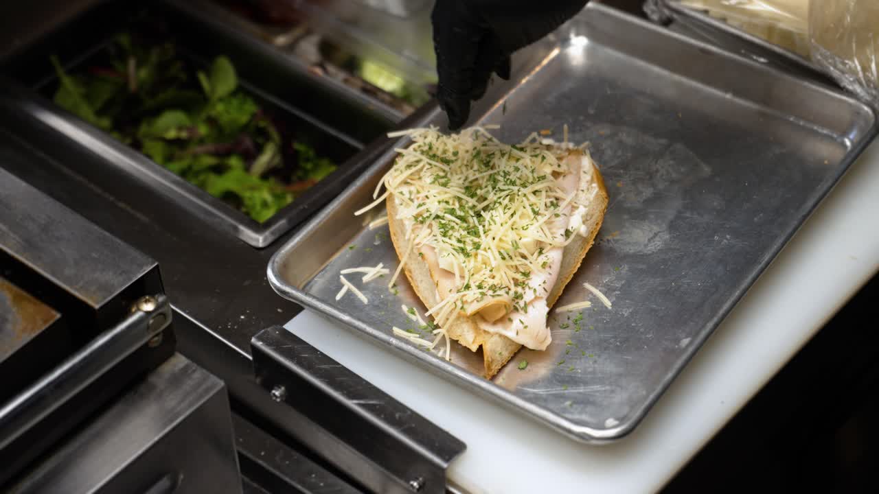 Chef sprinkles chopped chives over turkey brie parmesan sandwich on french bread before placing in oven, slow motion close up 4K