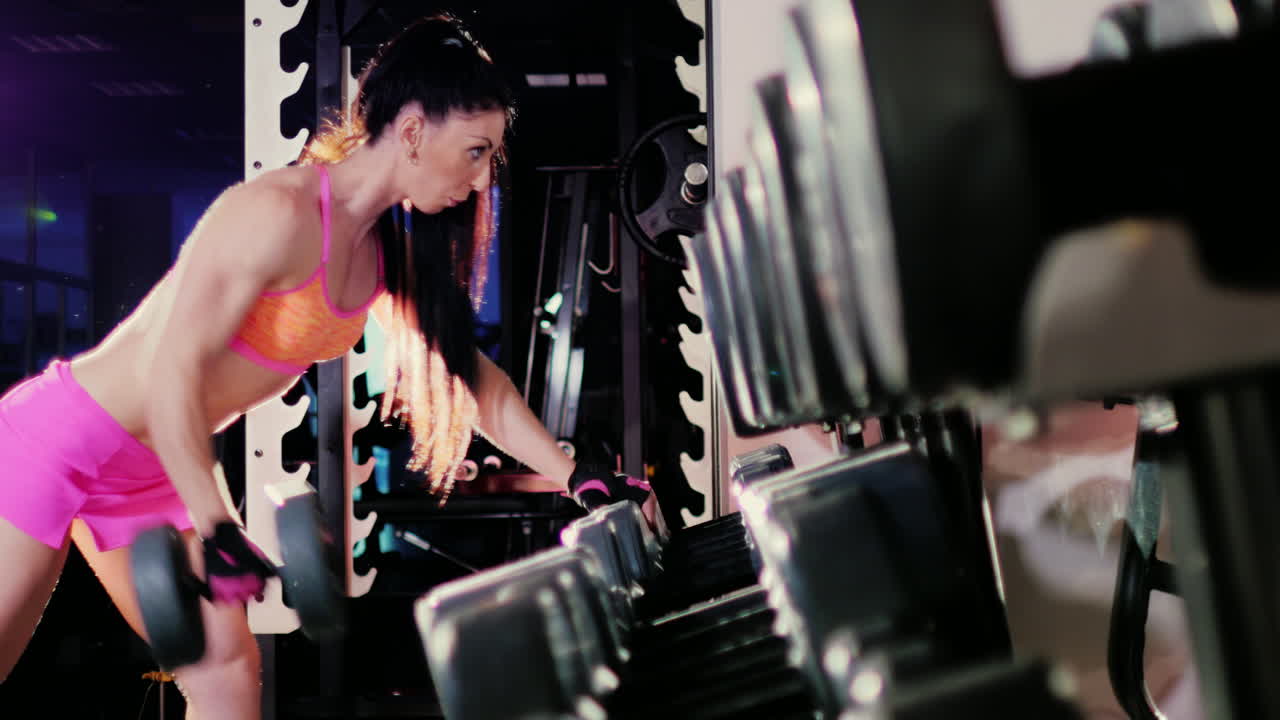 스포트라이트를 받으며 체육관에서 아령으로 운동을 하는 여성 운동선수