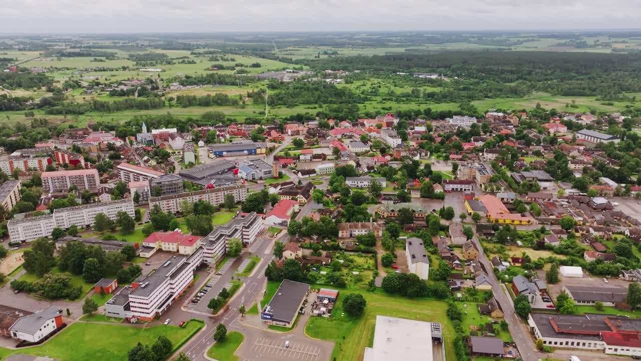 Drone flies sideways showing Latvian town Tukums with green fields and rooftops