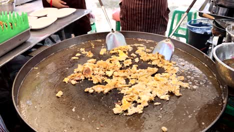 cooking scrambled eggs on a large outdoor griddle.