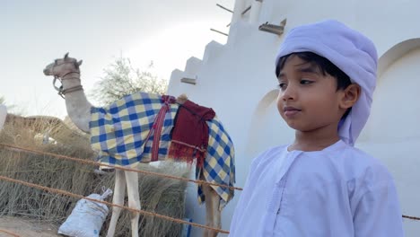 feliz niño emiratí sonriente y camello en el fondo tradicional