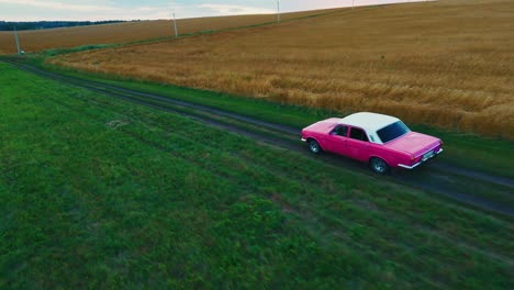 pink vintage car on a country road through a wheat field
