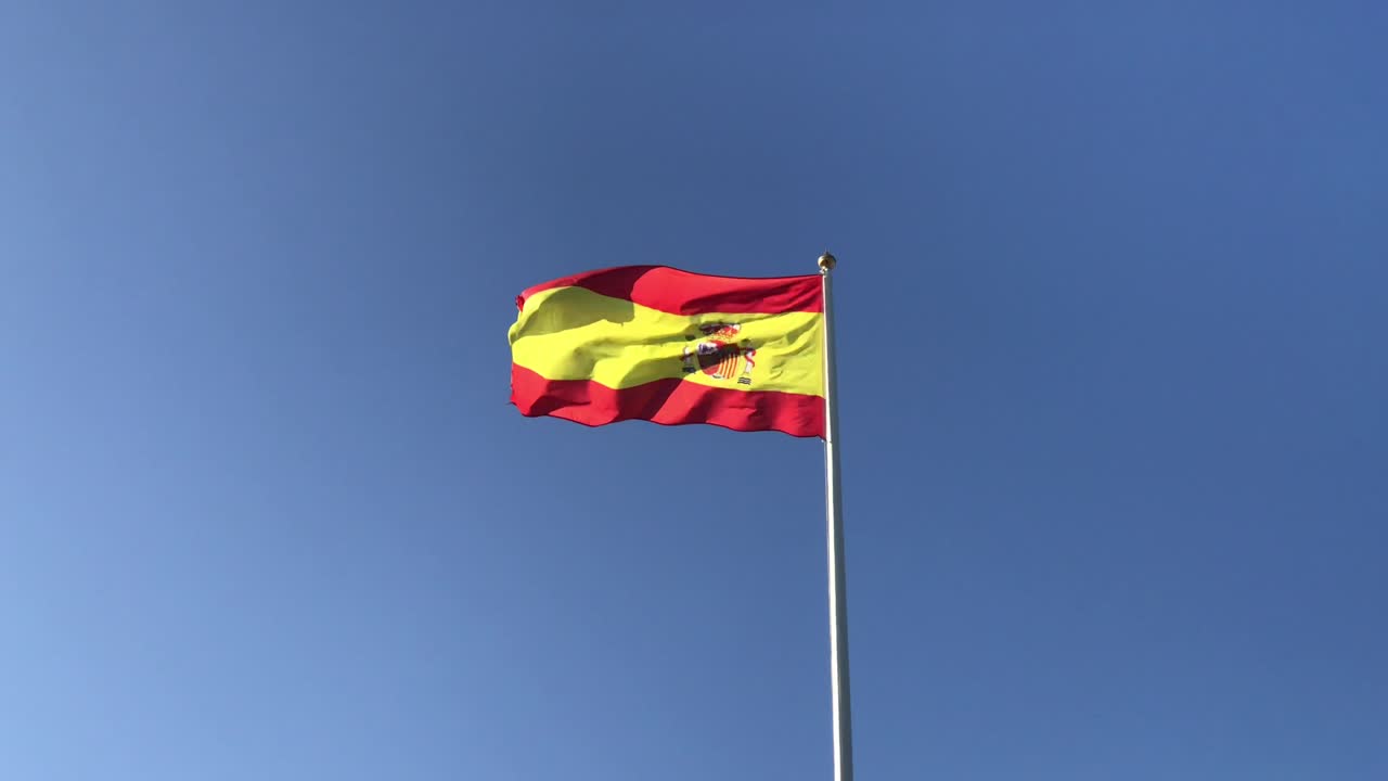 bandera nacional española en el poste ondeando en la naturaleza con cielo azul
